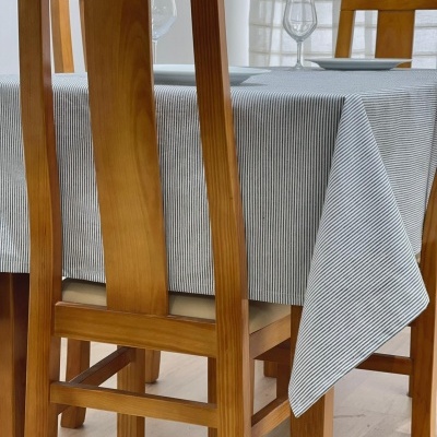 Cadeira de madeira castanha clara com mesa coberta por toalha às riscas cinzentas e brancas