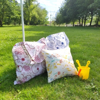 Três almofadas com padrões florais e balde de plástico amarelo na relva em parque