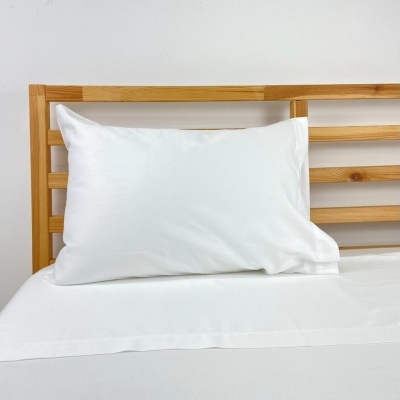 Almofada branca com fronha lisa em cama com cabeceira de madeira