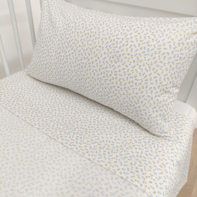 fronha e lençol com padrão floral azul, amarelo e verde sobre fundo branco em cama de estrutura metálica branca