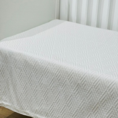 Cama com colcha branca com padrão geométrico de losangos em quarto simples