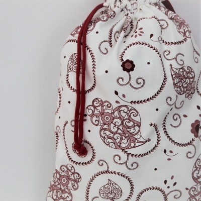 Saco de pano branco com padrão de corações e arabescos castanhos e cordão vermelho