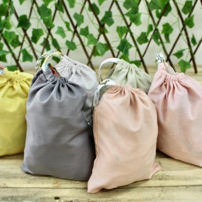 Cinco sacos de tecido coloridos com fecho em cordão sobre superfície de madeira