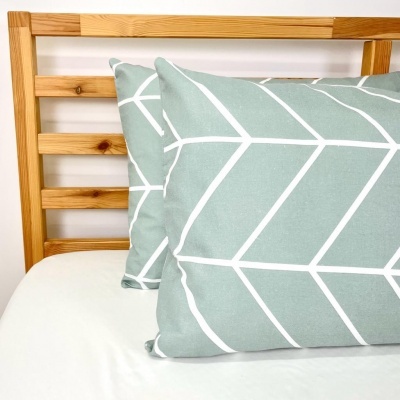 Capa de almofada verde-água com padrão branco de linhas geométricas numa cama com cabeceira de madeira