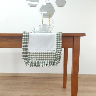 Guardanapo branco e verde às quadrículas pendurado numa mesa de madeira com chávenas empilhadas e espelhos hexagonais na parede