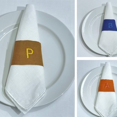 Guardanapos brancos com faixas coloridas e letras, sobre pratos brancos.