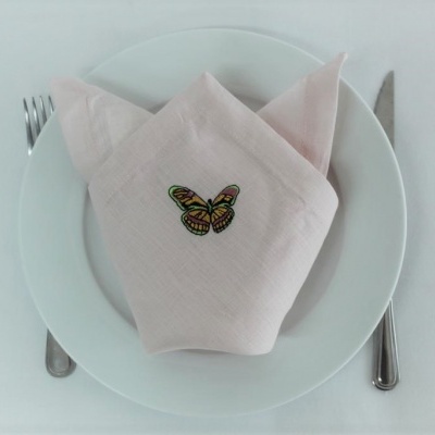 Guardanapo rosa claro com bordado de borboleta sobre prato branco