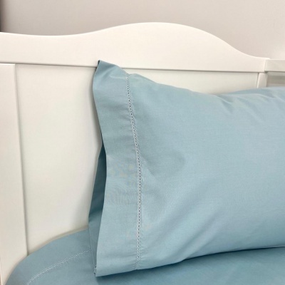 Fronha e lençol azuis claros sobre cabeceira branca de madeira