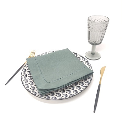 Conjunto de prato decorado, guardanapo verde, talheres cinza e dourado, e copo cinza transparente
