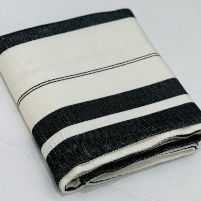 Toalha branca e preta com listras, dobrada sobre superfície branca.