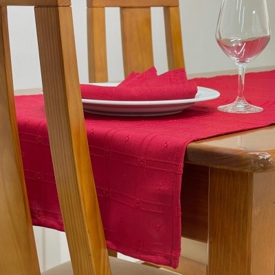 Mesa de madeira clara com toalha e guardanapo vermelhos, prato branco e taça de vinho vazia