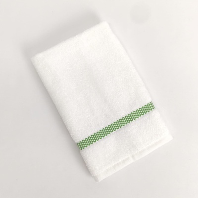 Toalha branca com faixa verde dobrada sobre fundo claro.