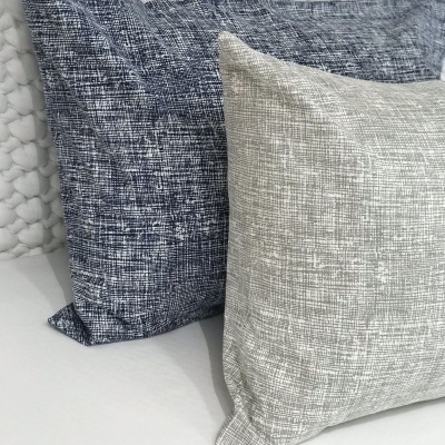 Três almofadas retangulares azul e cinza claro com texturas sobre cama branca.