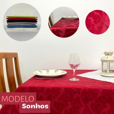 Toalha de mesa vermelha com padrão floral em relevo estendida sobre mesa com prato, copo e lanterna.