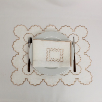 Jogo americano e guardanapo com bordados em branco e bege, prato branco, garfo e faca