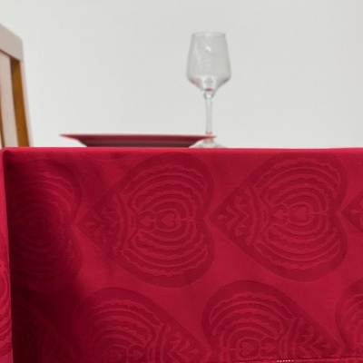 Toalha de mesa vermelha com padrão de corações, mesa de madeira e taça de vidro.