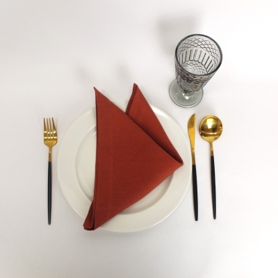 Conjunto de jantar com prato branco, guardanapo castanho, talheres dourados e pretos, copo de vidro com padrão geométrico