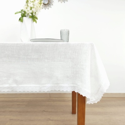 Toalha de mesa branca rendada sobre mesa de madeira com vaso, prato e copo