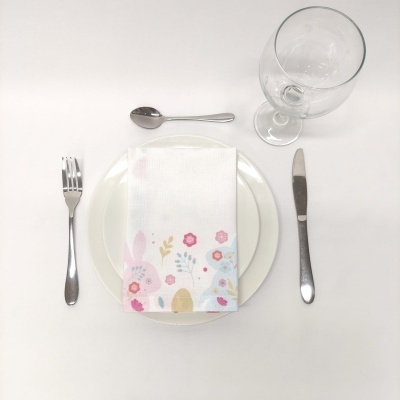 Conjunto de jantar com prato branco, talheres de metal, guardanapo com desenho de coelho e taça de vidro