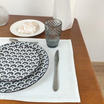 Conjunto de jantar com pratos decorados, copo cinza, talheres e guardanapo branco numa mesa de madeira.