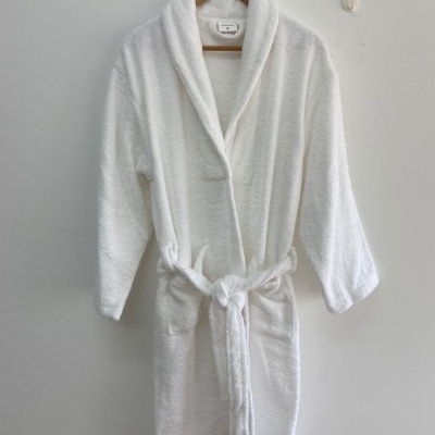 Robe de banho branco felpudo com cinto atado pendurado num cabide de madeira