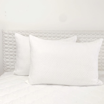 Duas almofadas brancas com padrão espinha sobre colchão branco acolchoado e cabeceira cinza claro acolchoada.