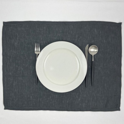 Prato branco com talheres de cabo preto sobre individual cinza escuro