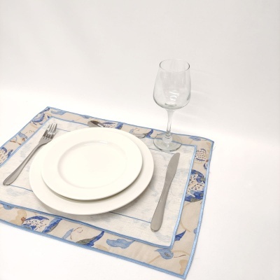 Conjunto de loiça com pratos, talheres e copo sobre individual de tecido azul e bege