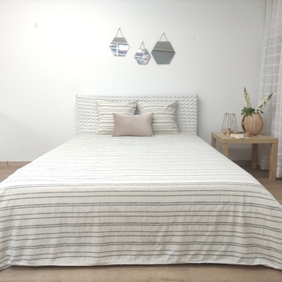 Cama com roupa de cama às riscas, almofadas, espelhos na parede e mesa de cabeceira com vaso e flores