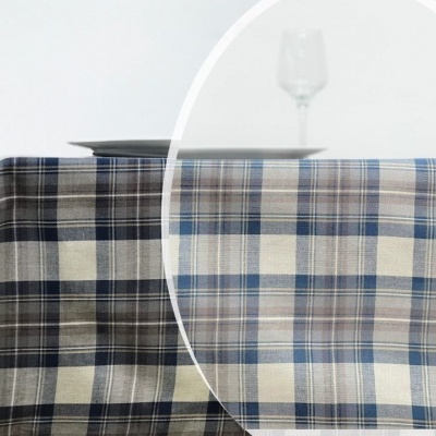 Toalha de mesa azul e cinzenta aos quadrados sobre uma mesa com cadeira de madeira e copo de vidro.