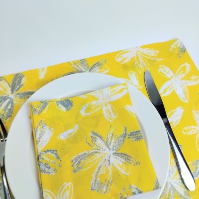 jogo americano e guardanapo amarelo com flores brancas e cinzas em prato branco com talheres