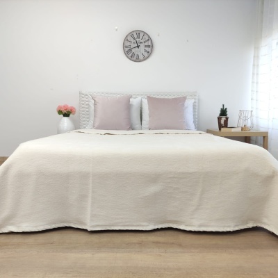 cama branca arrumada com almofadas rosa e brancas, relógio de parede, mesa de cabeceira com plantas e abajur