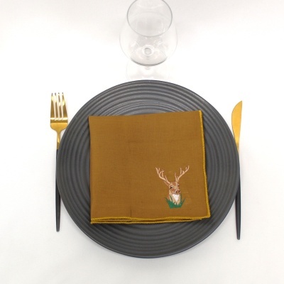 Prato cinzento texturado com guardanapo amarelo bordado, talheres dourados e pretos e copo