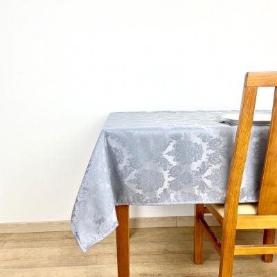 Toalha de mesa cinza com padrão floral numa mesa de madeira clara com cadeira de madeira ao lado