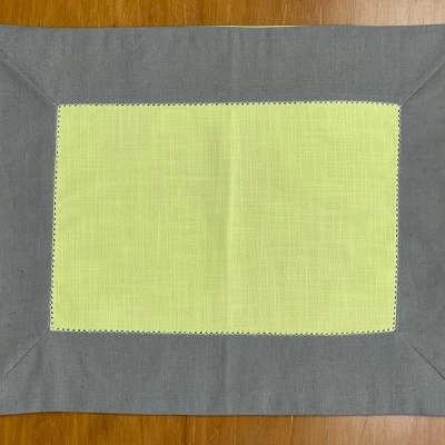 Individual de mesa retangular amarelo claro e cinza sobre mesa de madeira