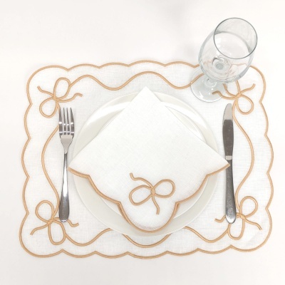 Conjunto de manta e guardanapo brancos com bordado castanho, utensílios de mesa e copo em superfície branca