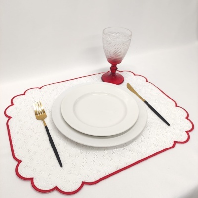 Conjunto de pratos brancos, copo texturizado, talheres preto e dourado sobre individual branco com borda vermelha