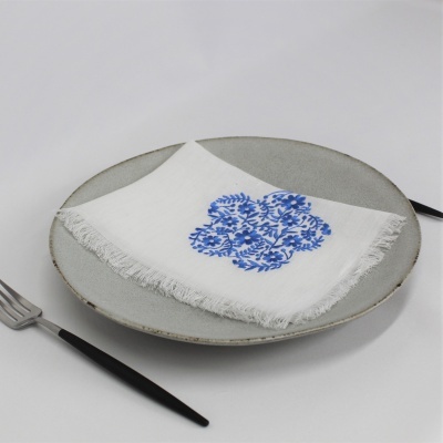 Guardanapo branco com padrão azul sobre prato cinza com talheres pretos