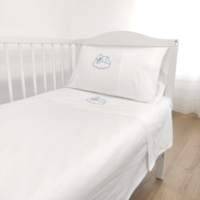Roupa de cama infantil branca com bordados azuis numa cama branca de grades