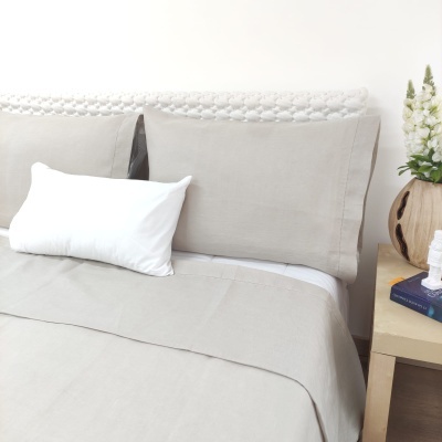 Conjunto de roupa de cama bege claro com fronhas e lençol junto a mesa-de-cabeceira com vaso e livros