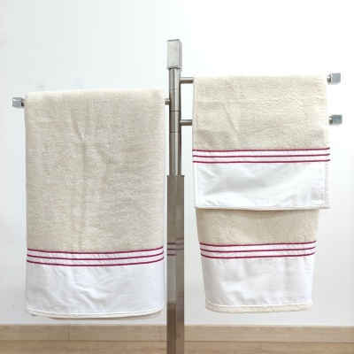 Conjunto de toalhas bege com faixa branca e riscas vermelhas penduradas num suporte metálico