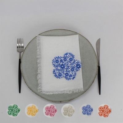 Prato cinzento com guardanapo branco bordado azul e talheres ao lado, com bordados coloridos em fila em baixo