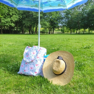 Guarda-sol azul, mochila floral e chapéu de palha sobre relva num parque