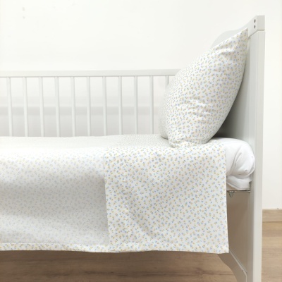 Cama branca com roupa de cama floral azul e amarela, almofada e chão de madeira