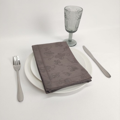 Conjunto de jantar com pratos brancos, guardanapo cinza, copo de vidro cinza e talheres prateados.