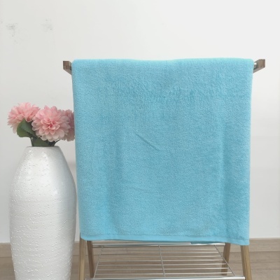 Toalha azul clara pendurada em estrutura de madeira ao lado de vaso branco com flores cor de rosa