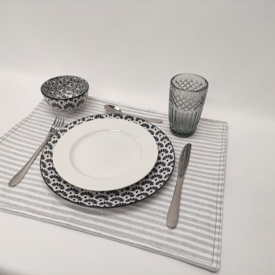 Conjunto de loiça com padrão floral preto e branco, copo cinzento texturizado e talheres sobre toalha cinzenta listrada.