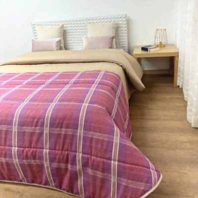 Cama de casal com roupa de cama e manta xadrez rosa, mesa de cabeceira e candeeiro