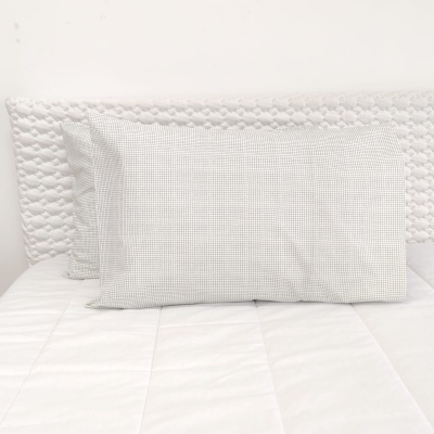 Almofadas com fronhas xadrez cinzento claro sobre cama branca com cabeceira almofadada branca