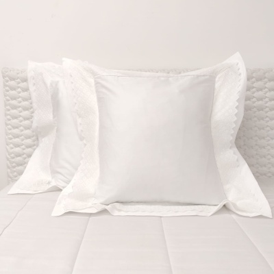 Almofada branca com bainha rendada sobre cama branca em fundo branco
